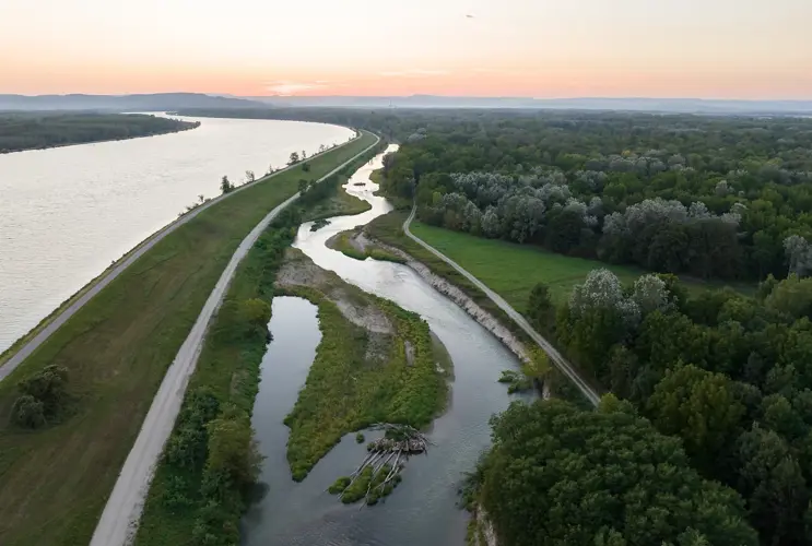 Blick auf die Fischwanderhilfe bei Wasserkraftwerkt Altenwörth bei Sonnenuntergang. Der Himmel ist in ein zartes Rosé getaucht.